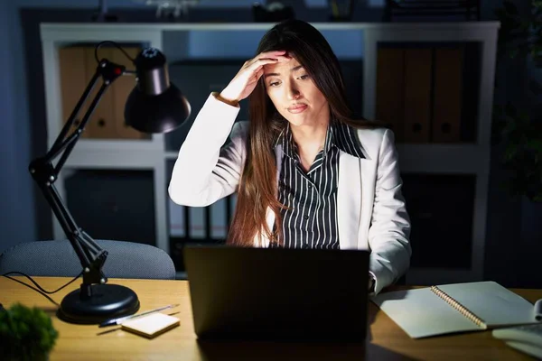若いブルネットの女性は夜のオフィスでラップトップを心配して仕事をし 額に手で問題について強調し 神経と危機への不安 — ストック写真