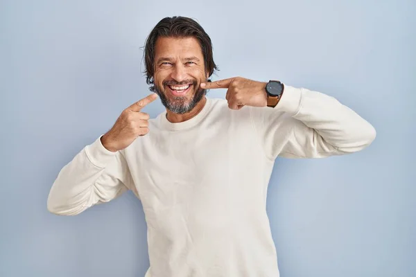 青い背景にカジュアルなセーターを着たハンサムな中年の男性が陽気な表情と指の歯と口で指して笑っています 歯の健康の概念 — ストック写真