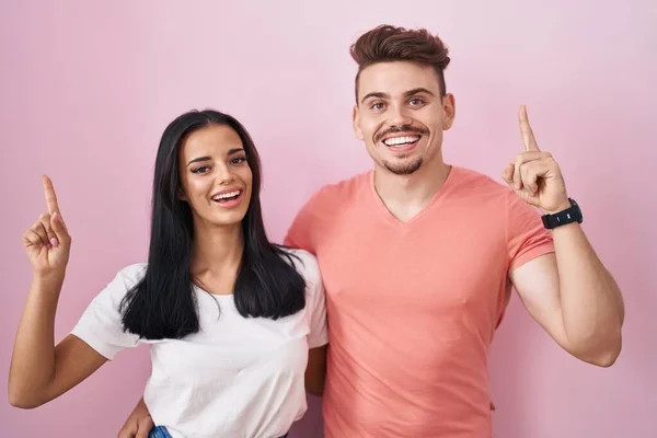Jong Hispanic Paar Staan Roze Achtergrond Lachend Verbaasd Verrast Wijzen — Stockfoto