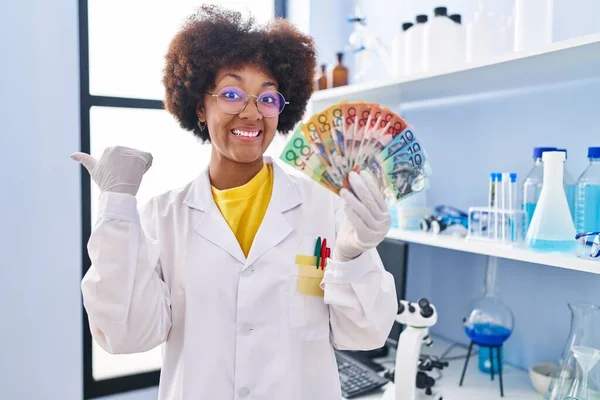 Joven Afroamericana Mujer Trabajando Laboratorio Científico Sosteniendo Dinero Apuntando Pulgar —  Fotos de Stock
