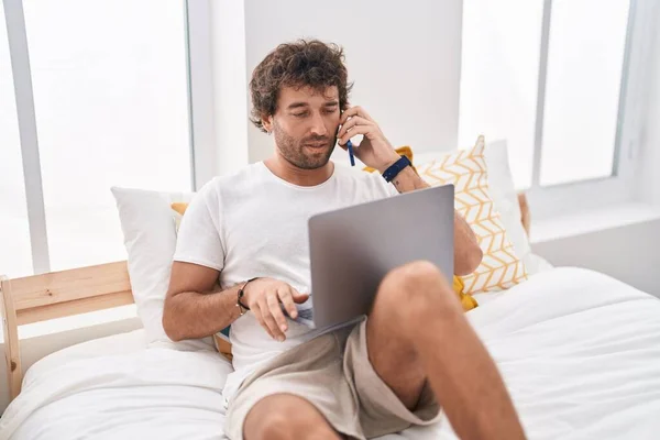 Young Hispanic Man Using Laptop Talking Smartphone Bedroom — Stock Photo, Image