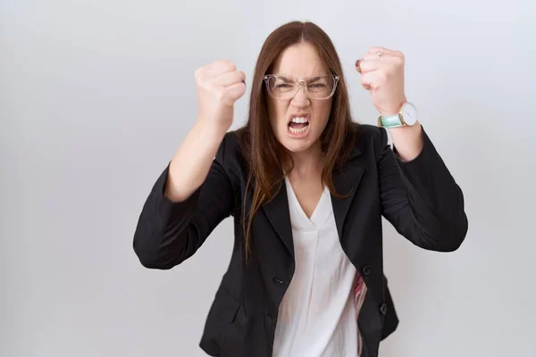 ビジネスジャケットとメガネを身に着けている美しいブルネットの女性は怒りで叫んでいる間に怒りと怒りに苛まれ 激怒した拳を上げる 怒りと攻撃的な考え方 — ストック写真