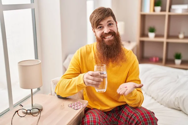 Young Redhead Man Taking Pills Drinking Water Sitting Bed Bedroom — Stok fotoğraf