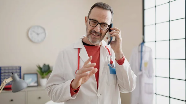 中年男人医生微笑着自信地在诊所用智能手机交谈 — 图库照片