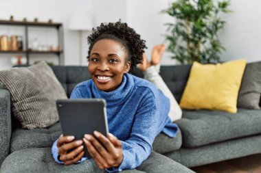 African american woman using touchpad lying on sofa at home