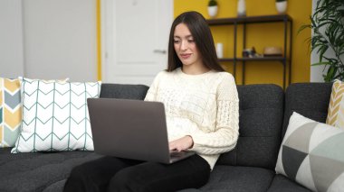 Evdeki kanepede dizüstü bilgisayar kullanan güzel İspanyol kadın.