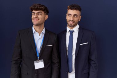 İki İspanyol iş adamı iş kıyafetleri giyip yüzünde gülümsemeyle yan yana bakıyorlar, doğal bir ifade. Kendinden emin gülen. 