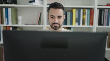 Young hispanic man student using computer studying at library university