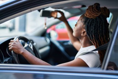 African american woman touching rearview sitting on car at street