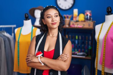 Young beautiful hispanic woman tailor smiling confident standing with arms crossed gesture at clothing factory