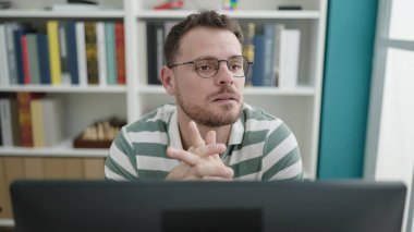 Young caucasian man using computer thinking at library university