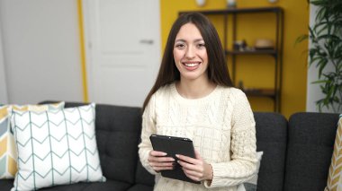 Evdeki kanepede oturan dokunmatik ped kullanan genç ve güzel İspanyol kadın.