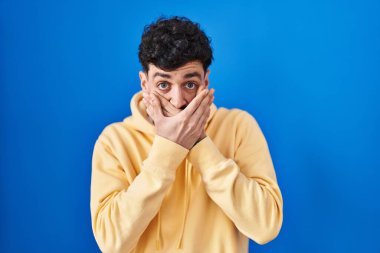 Mavi arka planda dikilen İspanyol adam yanlışlıkla ağzını kapatarak şok geçirdi. gizli kavram. 