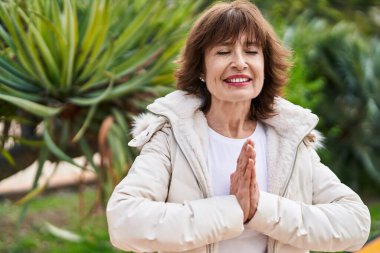 Orta yaşlı kadın parkta yoga egzersizi yapıyor.