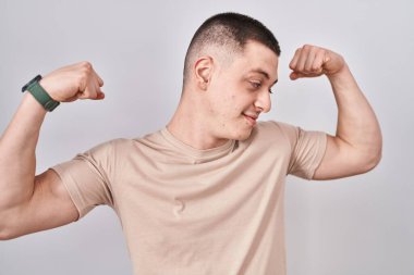 Young man standing over isolated background showing arms muscles smiling proud. fitness concept. 