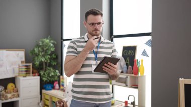 Young caucasian man working as teacher with tablet at kindergarten