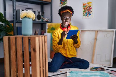 Young african american woman artist wearing headphones using touchpad at art studio