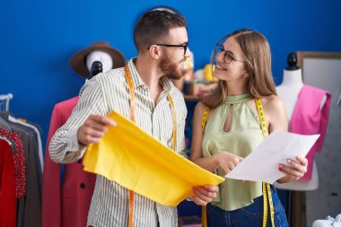 Man and woman tailors holding cloth looking clothing design at clothing factory