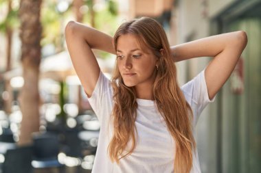 Sarışın genç kız, elleri başının üstünde ve sokakta ciddi bir ifadeyle rahatladı.