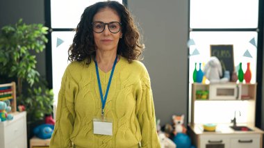 Orta yaşlı İspanyol kadın anaokulu öğretmeni anaokulunda rahat bir ifadeyle duruyor.