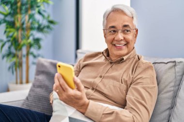 Senior man using smartphone sitting on sofa at home