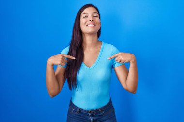 Mavi arka planda duran genç İspanyol kadın yüzünde bir gülümsemeyle kendine güveniyor, kendini gururlu ve mutlu bir şekilde gösteriyor.. 