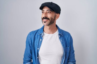 Sakallı İspanyol bir adam soyutlanmış arka planda duruyor. Yüzünde gülümseme, doğal bir ifade ile yan yana bakıyor. Kendinden emin gülen. 