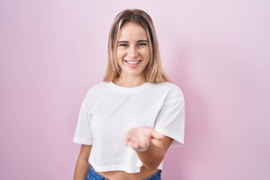 Pembe arka planda duran genç sarışın kadın mutlu bir şekilde gülümseyerek avuç içi yardım ve kabullenme teklif ediyor.. 