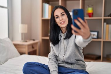 Young caucasian woman make selfie by smartphone sitting on bed at bedroom