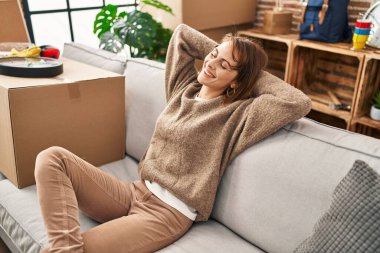 Kafkasyalı genç kadın, elleri başının üstünde, yeni evindeki kanepede oturuyor.