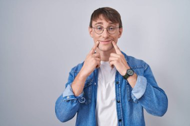 Beyaz, sarışın, gözlüklü, ağzı açık gülümseyen, parmakları işaret eden ve zorla gülümseyen bir adam. 