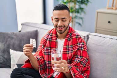 African american man taking pills sitting on sofa at home