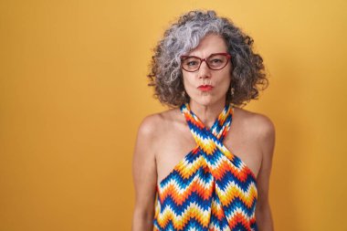 Sarı arka planda gri saçlı orta yaşlı bir kadın canlı yayında öpücük yollayan kameraya bakıyor. Güzel ve seksi. aşk ifadesi. 