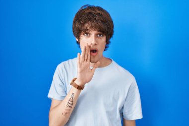 Latin kökenli genç bir adam mavi arka planda el ele tutuşup gizli söylentiler yayıyor, kötü niyetli konuşmalar fısıldıyor. 