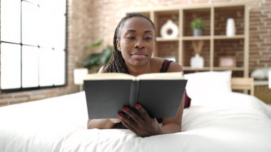 African woman reading book lying on bed at bedroom