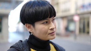 Genç Çinli kadın sokakta ciddi bir ifadeyle yan tarafa bakıyor.