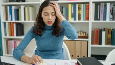 Üniversite sınıfındaki buruşuk kağıtların etrafında strese giren genç, güzel İspanyol bir bayan öğrenci.
