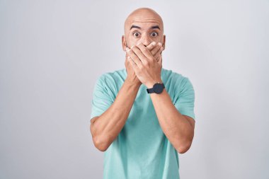 Beyaz arka planda duran orta yaşlı kel bir adam ağzının üstünü yanlışlıkla ellerle örterek şok etti. gizli kavram. 