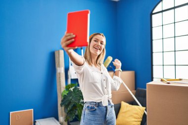 Latin kökenli genç bir kadın yeni evinde dokunmatik yastıkla selfie çekiyor.