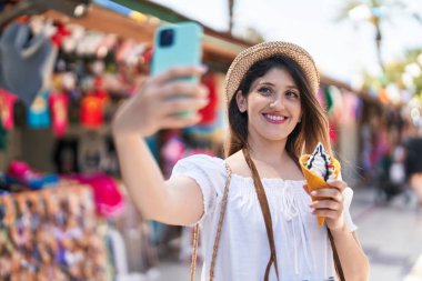 Dondurma yiyen genç İspanyol kadın turist, sokak pazarında akıllı telefondan selfie çekiyor.