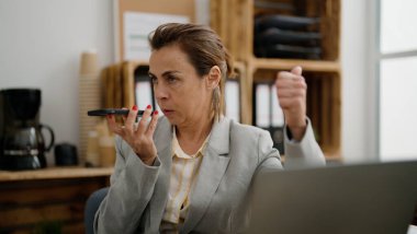 Orta yaşlı İspanyol iş kadını ofisteki akıllı telefondan konuşuyor.