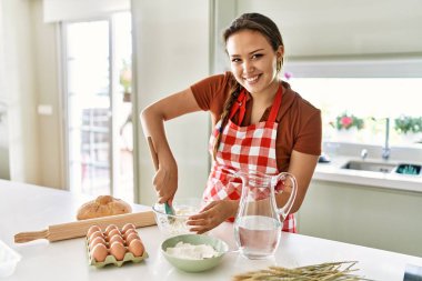 Genç ve güzel İspanyol kadın gülümsüyor. Mutfakta su ve unu karıştırıyor.