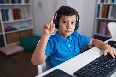 Okulda bilgisayar kullanan küçük İspanyol çocuk bir fikirle gülümsüyor ya da mutlu bir yüzle işaret ediyor. 