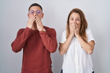 Anne ve oğlu izole arka planda bir arada durup gülüyor ve utanıyor kıkırdıyor ağızlarını ellerle, dedikodularla ve skandallarla örtüyor. 