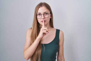 Beyaz arka planda dikilmiş beyaz tenli genç bir kadın sessiz olmak istiyor. sessizlik ve gizli konsept. 