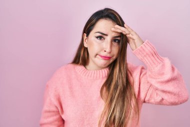 Young hispanic woman standing over pink background worried and stressed about a problem with hand on forehead, nervous and anxious for crisis 