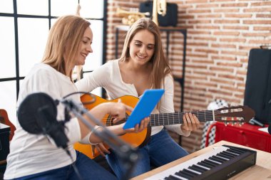Müzik stüdyosunda klasik gitar dersi alan iki kadın müzisyen.