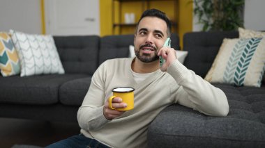 Genç İspanyol adam akıllı telefonda konuşuyor. Evde kahve içiyor.