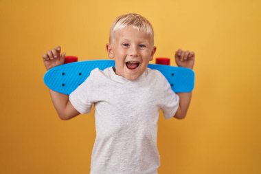 Küçük beyaz çocuk elinde paten tutarak çılgınlığı kutluyor ve başarıya hayret ediyor gözleri açık heyecanla bağırıyor.. 