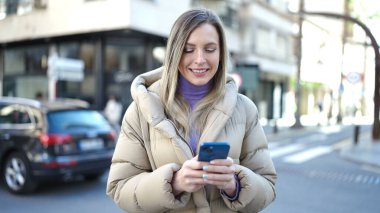 Sokakta akıllı telefon kullanan, kendine güvenen genç sarışın kadın.